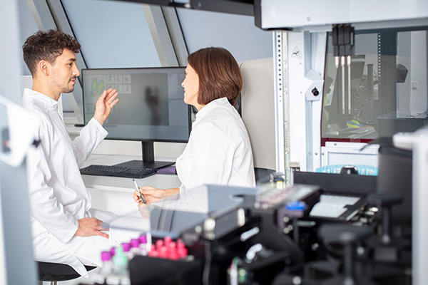 Flow cytometry lab personnel discussing the analysis results, while CellMek SPS is doing sample preparation.