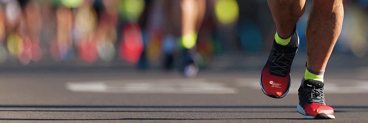 Cropped photo of the feet of the marathon runner, red shoes have Beckman Coulter Life Sciences logo on them